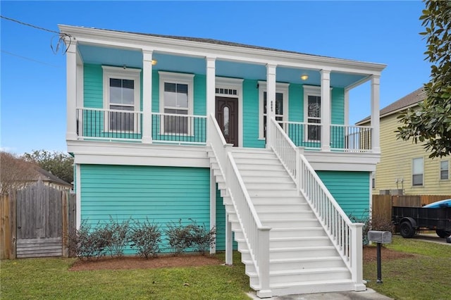 view of front of property with stairs, fence, covered porch, and a front yard