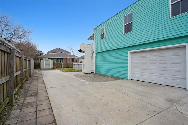 view of side of property featuring fence, an attached garage, a storage shed, an outbuilding, and concrete driveway