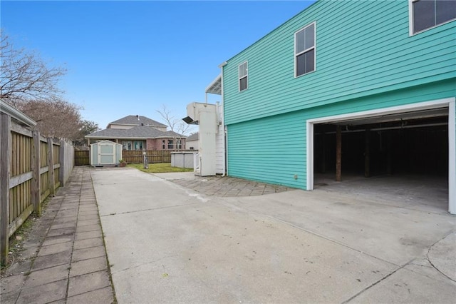 view of property exterior with a garage, fence, an outdoor structure, a storage unit, and concrete driveway