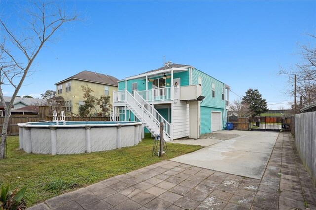 rear view of house with ceiling fan, driveway, stairway, a fenced in pool, and a yard