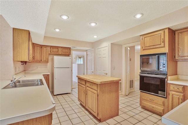 kitchen with a sink, a textured ceiling, light tile patterned floors, a kitchen island, and black appliances
