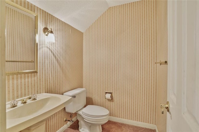 half bath with a sink, lofted ceiling, and wallpapered walls