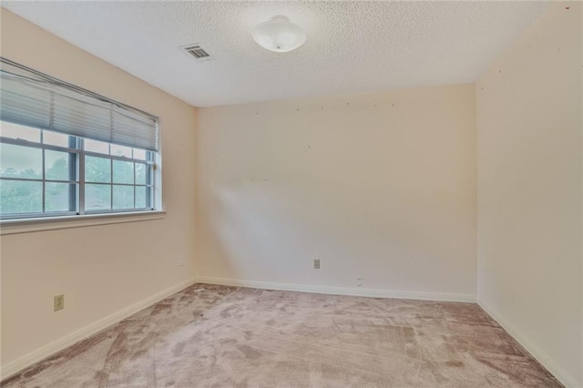 empty room with baseboards, visible vents, a textured ceiling, and light colored carpet