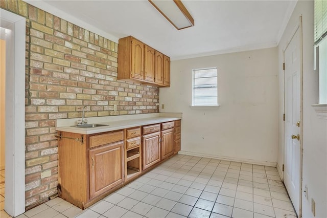kitchen featuring brown cabinetry, a sink, light countertops, light tile patterned floors, and ornamental molding
