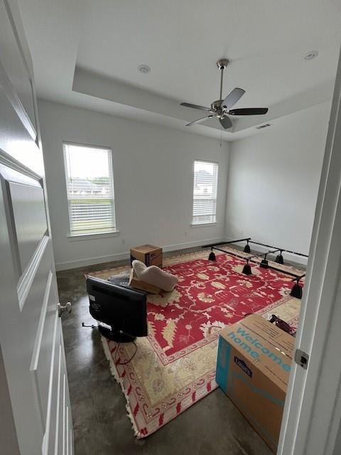 sitting room with baseboards, ceiling fan, a tray ceiling, and concrete floors