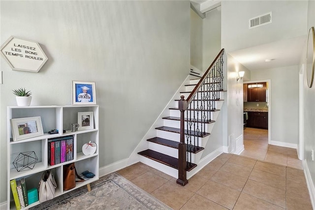 stairway with tile patterned floors, baseboards, a towering ceiling, and visible vents