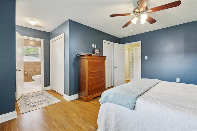bedroom featuring ceiling fan, visible vents, wood finished floors, baseboards, and multiple closets