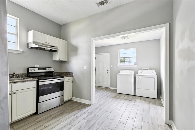 kitchen with electric range, dark countertops, under cabinet range hood, light wood-style flooring, and independent washer and dryer