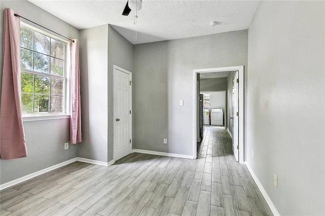 unfurnished bedroom with a textured ceiling, baseboards, multiple windows, and light wood-type flooring