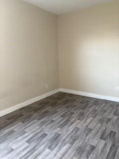 spare room with baseboards and dark wood-style floors