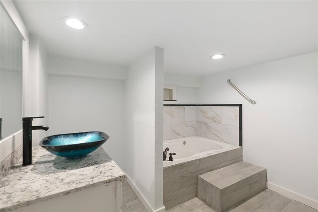 bathroom with a garden tub, vanity, wood finished floors, baseboards, and recessed lighting