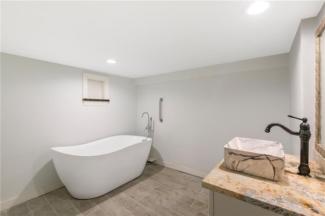 full bathroom featuring recessed lighting, baseboards, a freestanding bath, and vanity