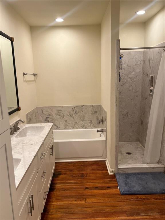 bathroom with a garden tub, double vanity, wood finished floors, a sink, and a stall shower