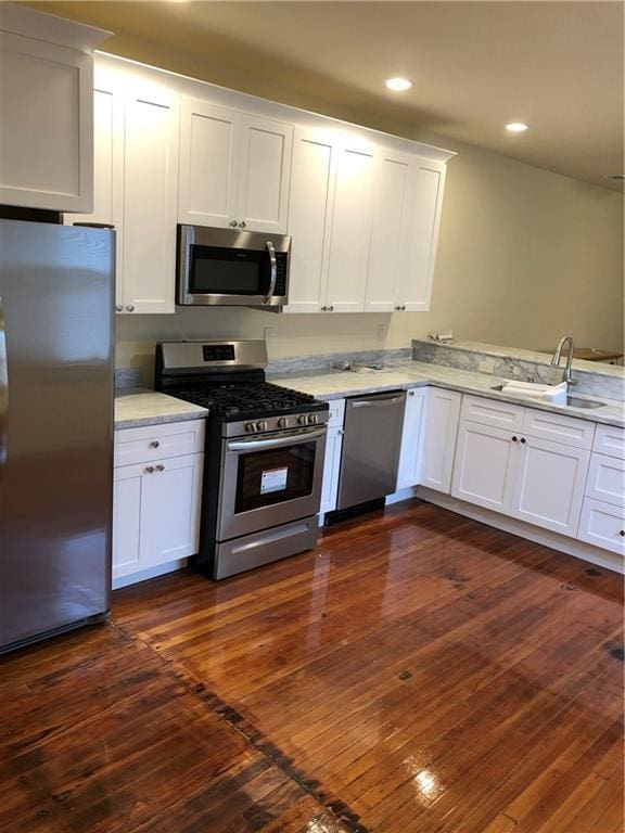 kitchen with a sink, stainless steel appliances, dark wood-style flooring, and white cabinetry