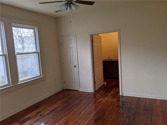 unfurnished bedroom featuring a ceiling fan, dark wood-style flooring, visible vents, a sink, and baseboards