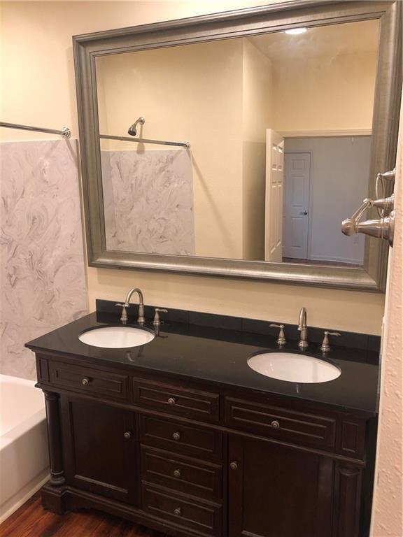 full bath with double vanity, wallpapered walls, a sink, and wood finished floors