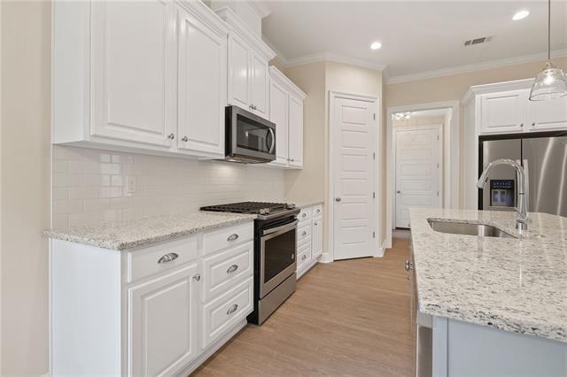 kitchen with ornamental molding, white cabinetry, a sink, light wood finished floors, and stainless steel appliances