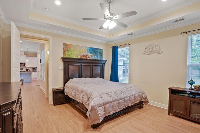 bedroom featuring ornamental molding, baseboards, light wood-type flooring, recessed lighting, and a tray ceiling
