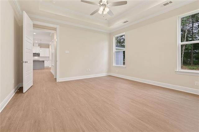 unfurnished room with a ceiling fan, baseboards, ornamental molding, a tray ceiling, and light wood-style flooring