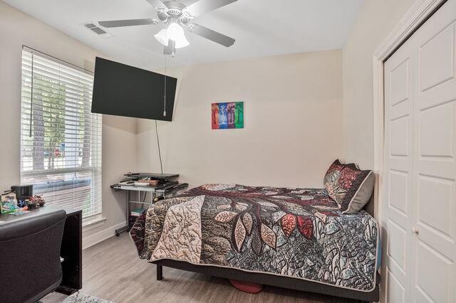 bedroom with a ceiling fan, baseboards, wood finished floors, visible vents, and a closet