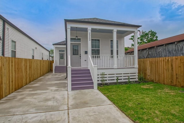 shotgun-style home featuring covered porch, fence, and a front lawn