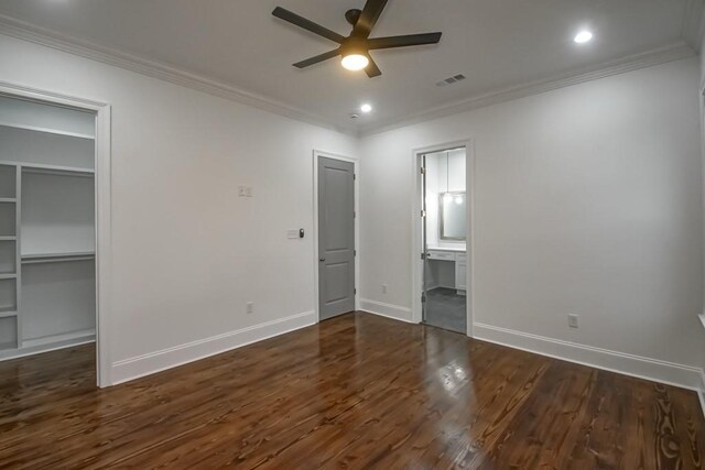 unfurnished bedroom with visible vents, crown molding, baseboards, a walk in closet, and dark wood-type flooring