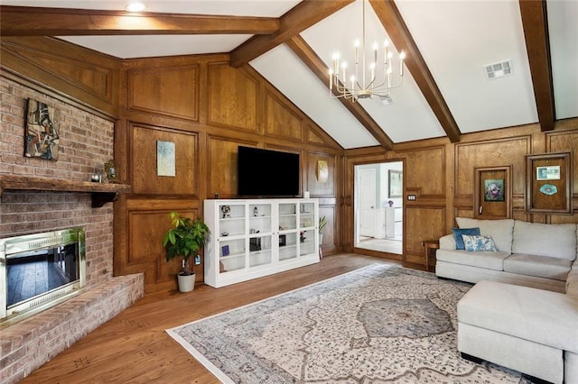 living area featuring visible vents, a fireplace, wood finished floors, an inviting chandelier, and vaulted ceiling with beams