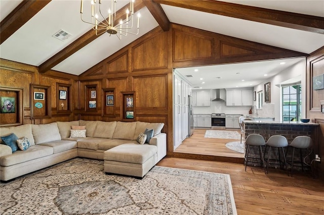 living area featuring visible vents, lofted ceiling with beams, wooden walls, a notable chandelier, and light wood-style floors