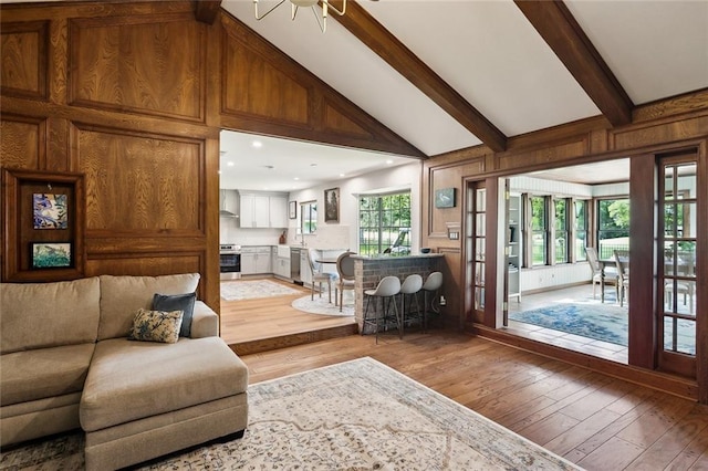 living room with lofted ceiling with beams, light wood finished floors, and wooden walls