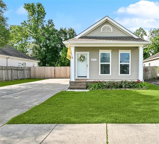 shotgun-style home with concrete driveway, fence, roof with shingles, and a front lawn