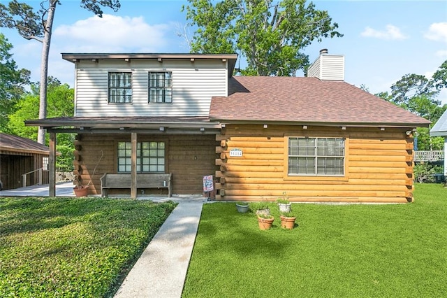 view of front of house featuring roof with shingles, log siding, a front yard, a chimney, and a patio area