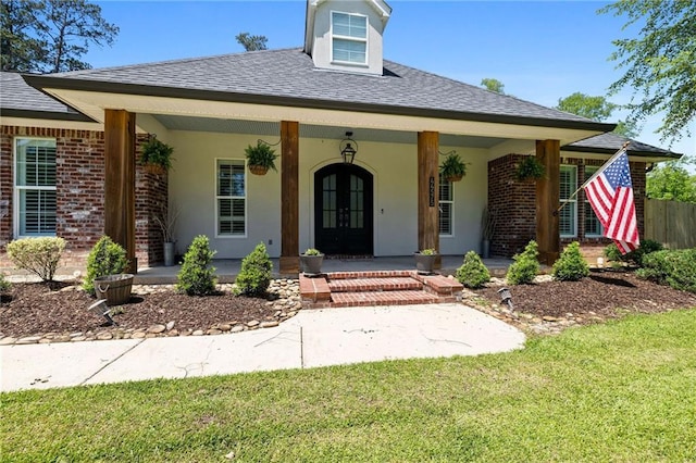 view of front of home featuring covered porch, brick siding, french doors, and a front yard