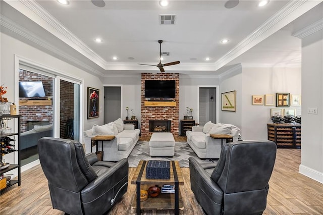 living area with visible vents, light wood-style floors, a brick fireplace, and a tray ceiling