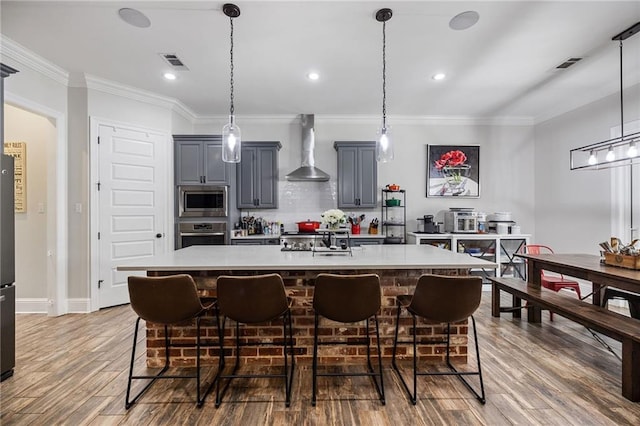 kitchen with visible vents, a kitchen breakfast bar, light countertops, wall chimney exhaust hood, and stainless steel appliances