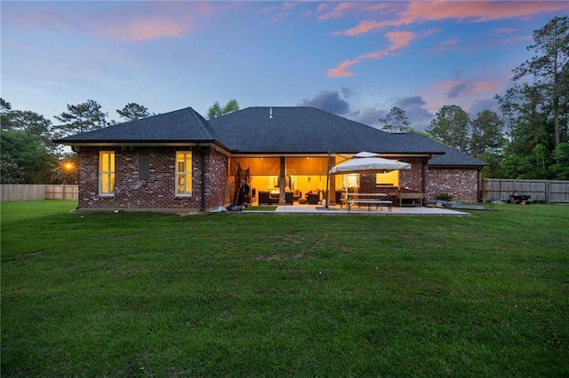 back of property at dusk with a lawn, brick siding, a patio, and a fenced backyard