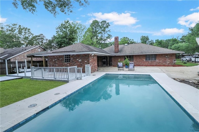 rear view of house with a chimney, brick siding, a fenced in pool, fence, and a yard