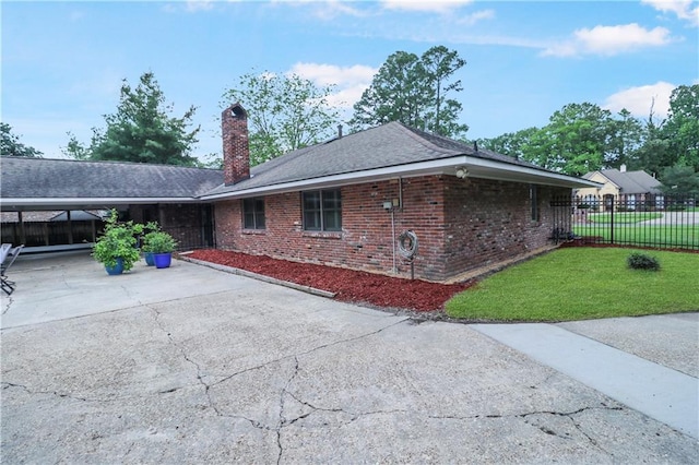 view of home's exterior featuring driveway, a carport, brick siding, fence, and a yard