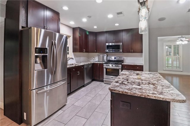 kitchen featuring a kitchen island, dark brown cabinets, light stone countertops, a sink, and appliances with stainless steel finishes