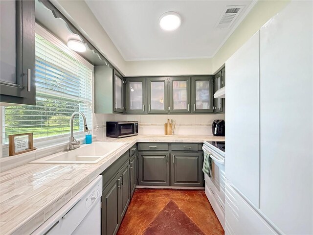 kitchen with a sink, white appliances, gray cabinets, visible vents, and glass insert cabinets