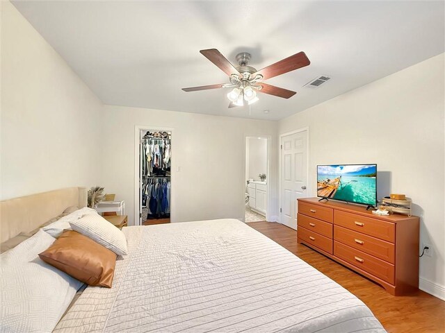 bedroom with a ceiling fan, visible vents, wood finished floors, baseboards, and a spacious closet