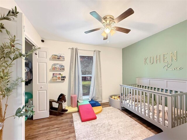 bedroom with a crib, baseboards, a ceiling fan, and wood finished floors