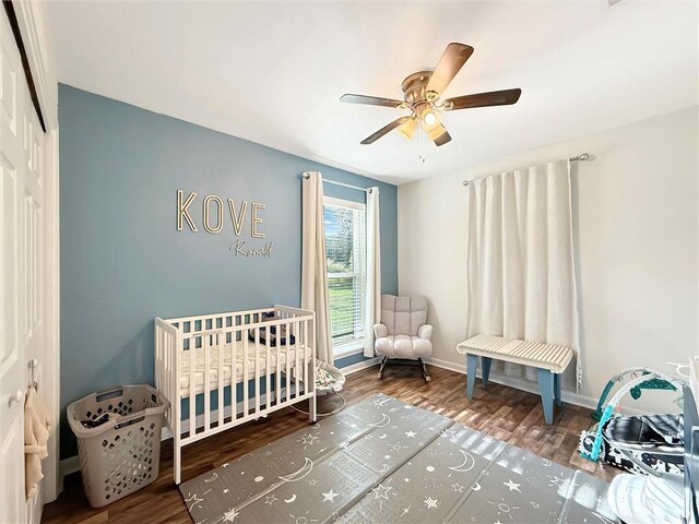 bedroom featuring a crib, a ceiling fan, baseboards, wood finished floors, and a closet