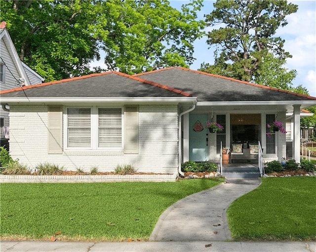 view of front of house with a porch, brick siding, roof with shingles, and a front lawn