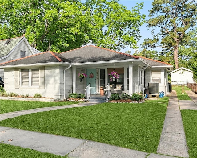 view of front of property featuring brick siding, central air condition unit, covered porch, and a front yard