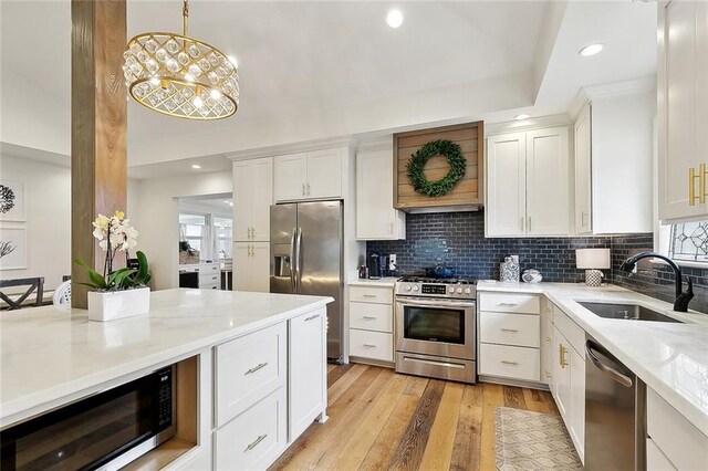 kitchen featuring backsplash, decorative light fixtures, appliances with stainless steel finishes, a sink, and white cabinetry