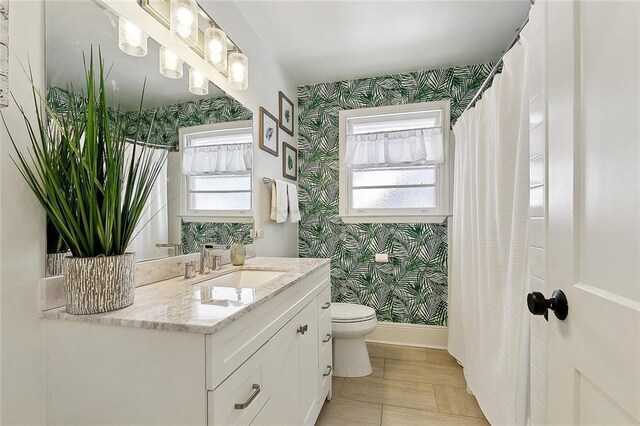 full bath with a healthy amount of sunlight, vanity, toilet, and wallpapered walls