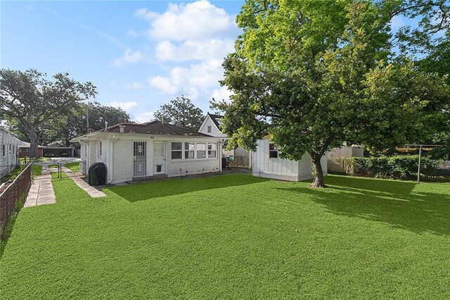 rear view of property featuring fence, an outdoor structure, and a yard