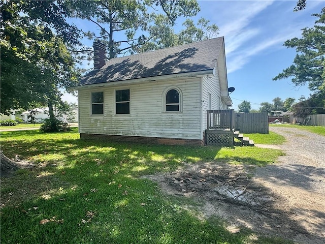 view of side of home featuring driveway, roof with shingles, a yard, and a chimney