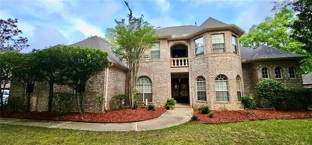 french provincial home with a balcony, a front lawn, and brick siding