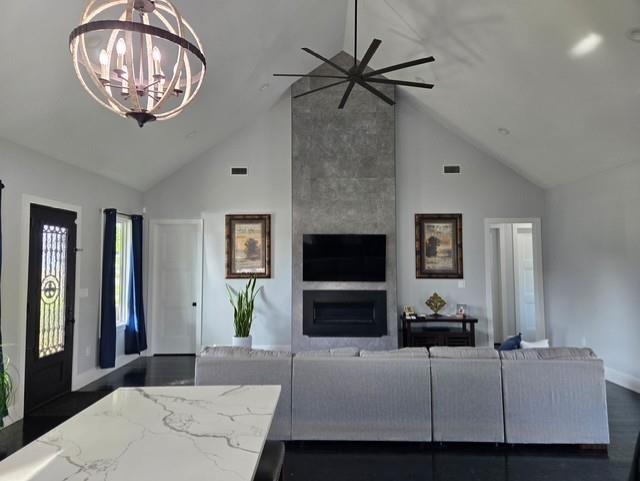living area featuring high vaulted ceiling, a fireplace, ceiling fan with notable chandelier, and visible vents